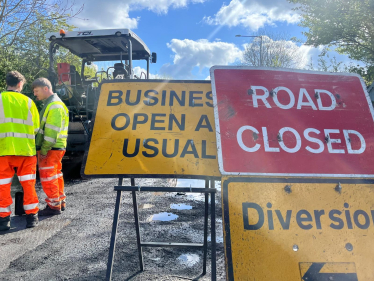 Road resurfacing work with road signs and workers visible