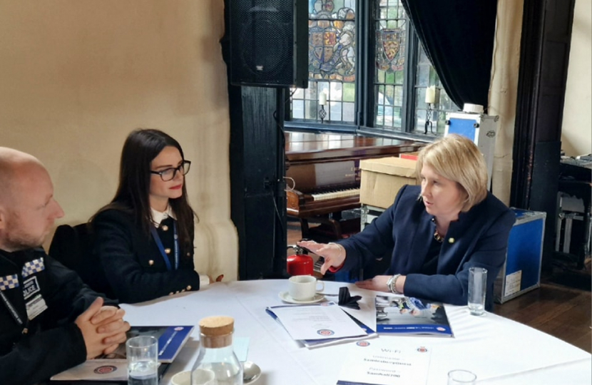 Katherine Fletcher at a round table with a woman and a police officer. Material relating to the meeting is scattered across the table and they are deep in conversation.
