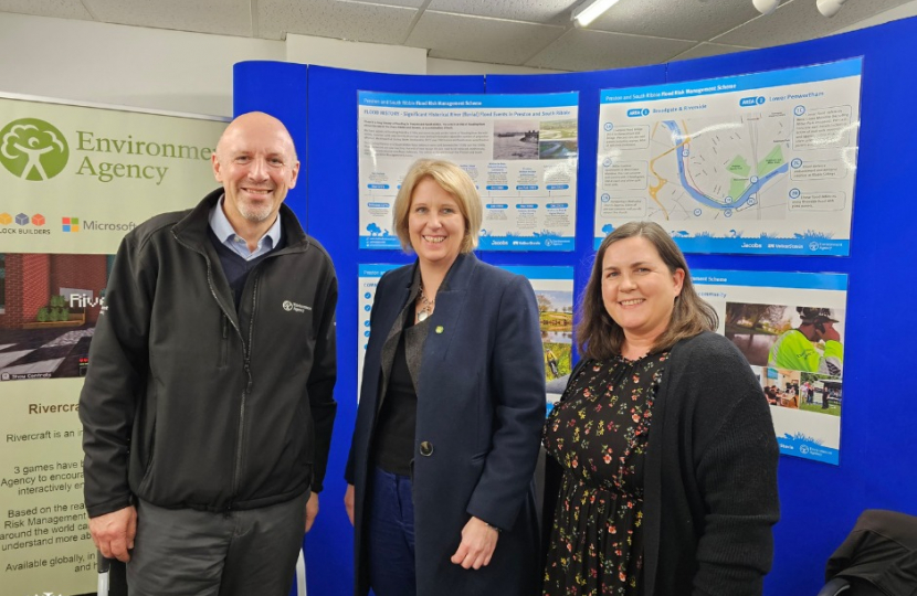 Katherine Fletcher stood with two members of the Environment Agency. An information board about the flood scheme is behind them.
