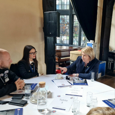 Katherine Fletcher at a round table with a woman and a police officer. Material relating to the meeting is scattered across the table and they are deep in conversation.